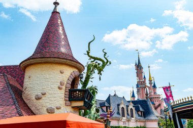 Bir lunaparktaki kale binalarının manzarası. Bronz bir kule ve fasulye sırığı heykeli ön planda, Disneyland Paris 'in arka planında pembe bir şato var..