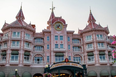 Pembe ve beyaz Disneyland Park otel cephesi saat kulesi ve parlak bir gökyüzünün altında kemerli giriş tabelası olan Disneyland Paris 'te..