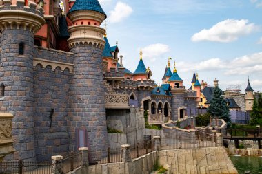 Taş duvarları, mavi ve pembe taretleri ve kısmen bulutlu bir günde Disneyland Paris 'te hendeği olan bir kalenin dış görüntüsü..