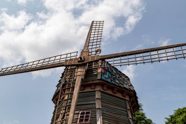 Renkli kiremitleri olan ahşap bir yel değirmeninin alçak açılı çekimi, beyaz bulutlu parlak bir gökyüzüne karşı kurulmuş. Yel değirmeni, Disneyland Paris 'in en önemli unsurudur..