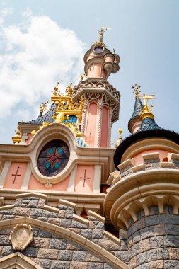 Low-angle shot of Sleeping Beauty's Castle at Disneyland Paris, showcasing pink and gray stonework against a partly cloudy sky.