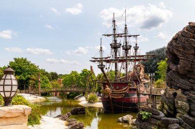 Rıhtıma yanaşmış bir korsan gemisi görüyorum. Etrafı yemyeşil, köprü, kaya oluşumu ve Disneyland Paris 'te eski moda bir fenerle çevrili..