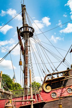 Beyaz bulutlu mavi gökyüzüne karşı alçak açılı bir korsan gemisi direği, teçhizat, ahşap işçiliği ve Disneyland Paris 'teki detaylı dekorasyonlara odaklanıyor..