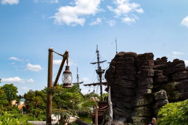 Bir korsan gemisinin manzarası kayalık bir oluşum ve ahşap bir lamba direğinin arkasında, mavi gökyüzünün altında dağınık bulutlarla Disneyland Paris 'te.