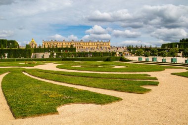 Paris, Versailles Sarayı 'nda parçalı bulutlu bir gökyüzünün altında saraya ve Orangerie' ye uzanan geometrik çimenli ve çakıl yollu Versailles bahçeleri..