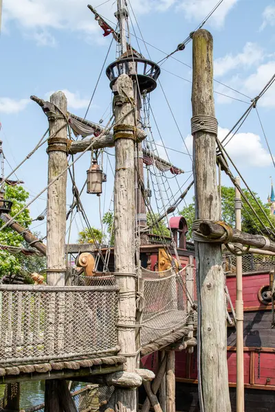 Direkleri, donanımları, platformları ve ip köprüleri olan ahşap bir korsan gemisinin görüntüsü Disneyland Paris 'te dağınık bulutlarla mavi bir gökyüzüne kurulmuş..
