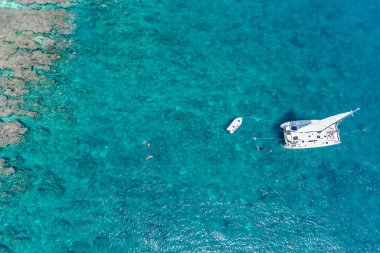Tropikal turkuaz okyanus sularındaki güzel yelkenli yatının havadan görünüşü. Yazın duvar kağıdında parlak, güneşli bir gün. Deniz manzaralı arka plan. Kıyı duvar kağıdı.