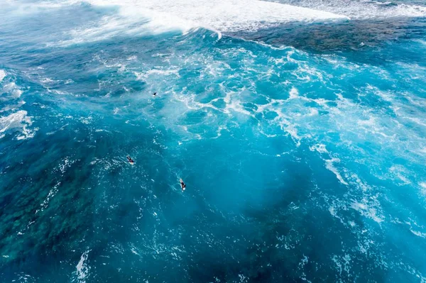 Big sea waves and dark blue water. Surfers paddling out in big surf.
