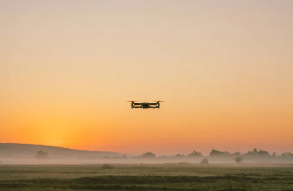 Gün batımında bir tarlada uçan bir dronun silueti..