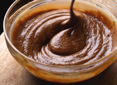 Kalın ve parlak zencefilli kurabiye hamuru cam kasede kaşıkla karıştırılıyor. Pürüzsüz koyu kahverengi vuruşlu fırın işlemini gösteren yakın çekim görüntüsü.