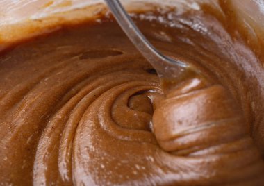 Cam kasede yumuşak ve kremalı zencefilli kurabiye hamuru kaşıkla karıştırılıyor. Pürüzsüz doku ve zengin kahverengi renk yakın planda vurgulanmış.