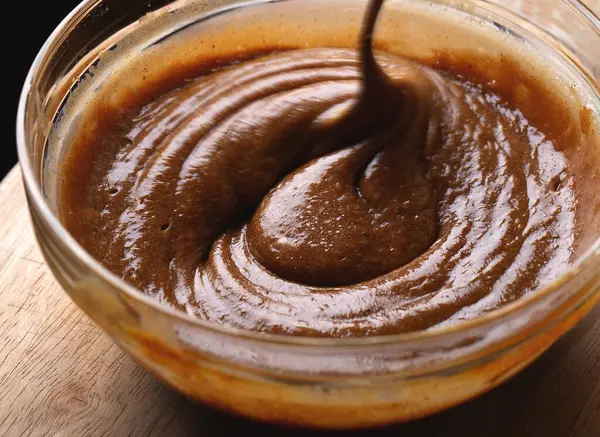 Kalın ve parlak zencefilli kurabiye hamuru cam kasede kaşıkla karıştırılıyor. Pürüzsüz koyu kahverengi vuruşlu fırın işlemini gösteren yakın çekim görüntüsü.