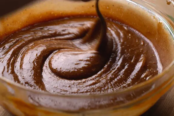 Kalın ve parlak zencefilli kurabiye hamuru cam kasede kaşıkla karıştırılıyor. Pürüzsüz koyu kahverengi vuruşlu fırın işlemini gösteren yakın çekim görüntüsü.