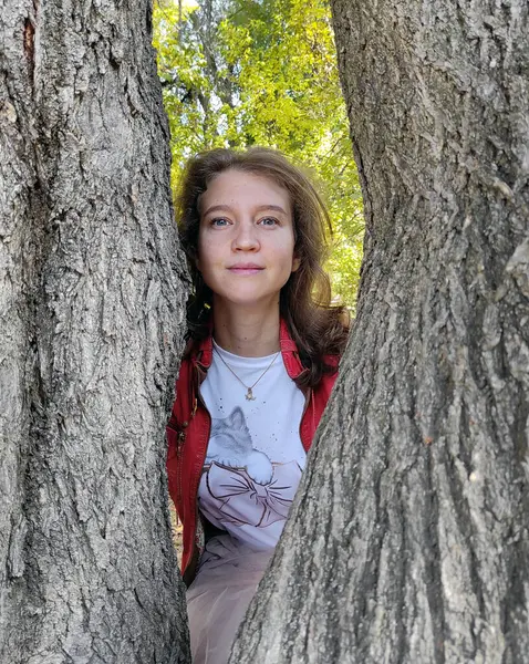 Genç bir kız ağaç gövdelerinin arasında dikiliyor.