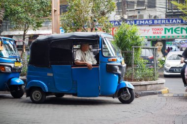 Mavi bir Bajaj şoförü Blok M Mall Jakarta 'nın önünde yolcuları bekliyor.