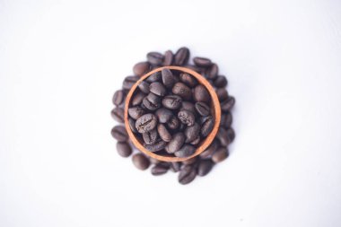 Kahve çekirdekleri beyaz bir masada, tahta bir kasede.