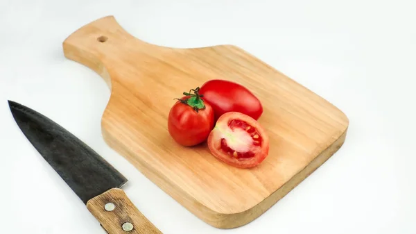 Stock image Pile of tomatoes on a wooden board some sliced with a knife. Ripe tomatoes with cut lines. Organic fresh tomatoes isolated on white.