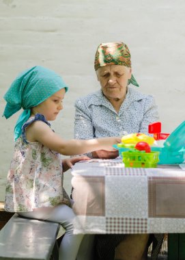 Küçük bir kız bahçedeki bir köyde yaşlı bir kadınla masa oyunu oynuyor. Birlikte eğlenmenize bakın. Büyükannem ve torunumla aile ilişkisi..
