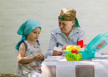 Küçük bir kız bahçedeki bir köyde yaşlı bir kadınla masa oyunu oynuyor. Birlikte eğlenmenize bakın. Büyükannem ve torunumla aile ilişkisi..