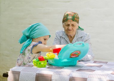 Küçük bir kız bahçedeki bir köyde yaşlı bir kadınla masa oyunu oynuyor. Birlikte eğlenmenize bakın. Büyükannem ve torunumla aile ilişkisi..