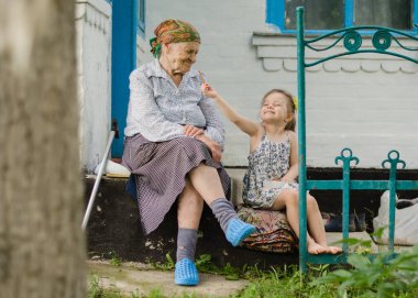Küçük bir kız ve yaşlı bir kadın eski evlerinin merdivenlerinde oturuyorlar. Küçük bir kız pipet bisküvi yer ve büyükannesiyle paylaşır. Ukrayna köyü. Büyükannem ve torunumla aile ilişkisi..