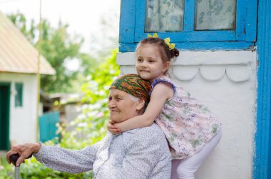 Küçük bir kız yaşlı büyükannesine sıkıca sarılıyor ve gülüyor. Ukrayna köyü. Büyükannemle torunum arasındaki ilişki.