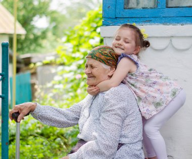Küçük bir kız yaşlı büyükannesine sıkıca sarılıyor ve gülüyor. Ukrayna köyü. Büyükannemle torunum arasındaki ilişki.