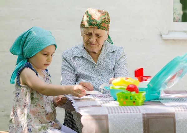 A little girl plays a board game with an older woman in a village in the yard. Have fun together. Family relationship with grandmother and granddaughter.