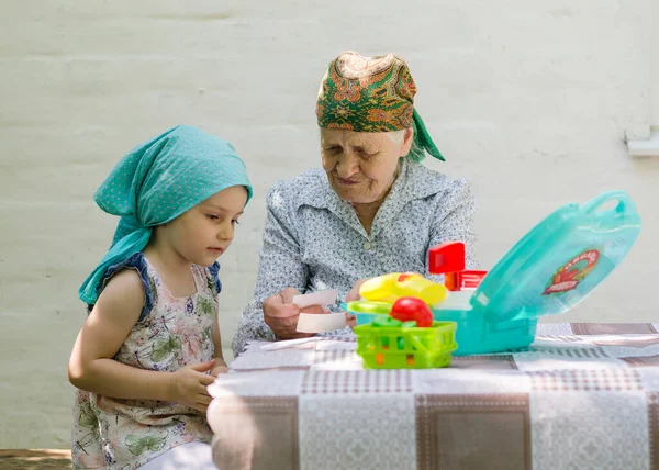 A little girl plays a board game with an older woman in a village in the yard. Have fun having fun together. Family relationship with grandmother and granddaughter.