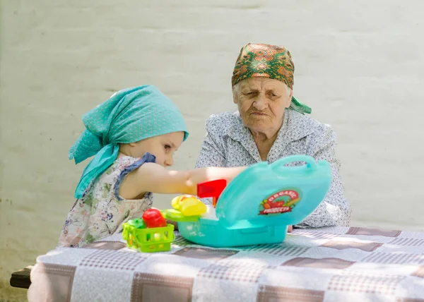 Küçük bir kız bahçedeki bir köyde yaşlı bir kadınla masa oyunu oynuyor. Birlikte eğlenmenize bakın. Büyükannem ve torunumla aile ilişkisi..