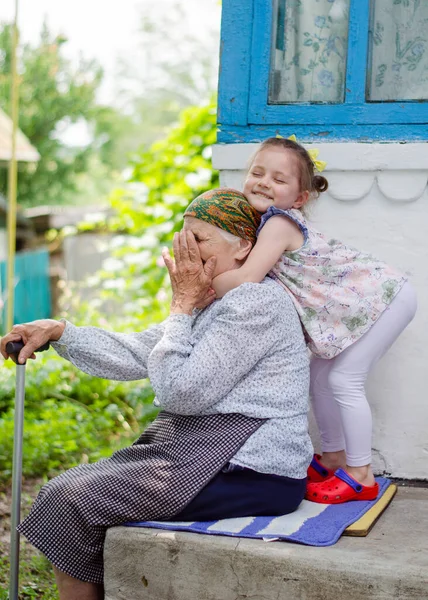 Küçük bir kız yaşlı büyükannesine sıkıca sarılıyor ve gülüyor. Ukrayna köyü. Büyükannemle torunum arasındaki ilişki.