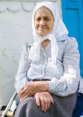 Yaşlı bir kadının portresi. Bir kadın (90 yaşında) gülümser ve evin yanında oturur. Ukraynalı yaşlı kadın, Ukrayna köyü. Açık hava.