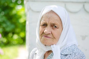 Yaşlı bir kadının portresi. Bir kadın (90 yaşında) gülümser ve evin yanında oturur. Ukraynalı yaşlı kadın, Ukrayna köyü. Açık hava.