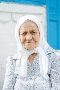 Yaşlı bir kadının portresi. Bir kadın (90 yaşında) gülümser ve evin yanında oturur. Ukraynalı yaşlı kadın, Ukrayna köyü. Açık hava.
