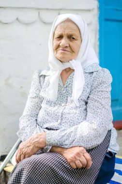 Yaşlı bir kadının portresi. Bir kadın (90 yaşında) gülümser ve evin yanında oturur. Ukraynalı yaşlı kadın, Ukrayna köyü. Açık hava.