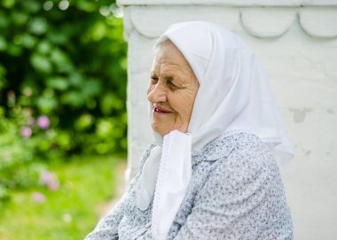 Yaşlı bir kadının portresi. Bir kadın (90 yaşında) gülümser ve evin yanında oturur. Ukraynalı yaşlı kadın, Ukrayna köyü. Açık hava.