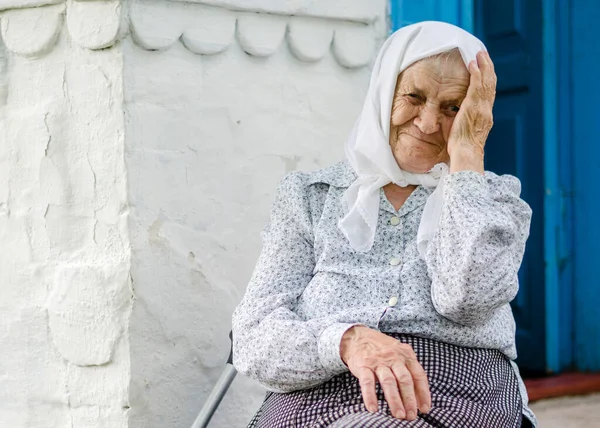 Yaşlı bir kadının portresi. Bir kadın (90 yaşında) gülümser ve evin yanında oturur. Ukraynalı yaşlı kadın, Ukrayna köyü. Açık hava.