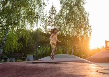 Gün batımında çocuk parkında mutlu bir kız. Kız trambolinde zıplıyor..