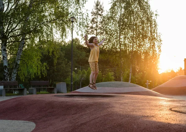 stock image A happy girl at a playground during sunset. The girl is jumping on a trampoline.