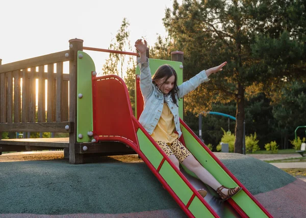 stock image A happy girl at a playground during sunset. The girl is sliding down a slide.