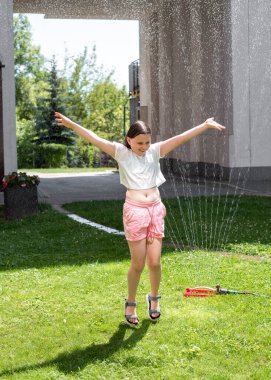 Sıcak bir yaz gününde bir kız fıskiyenin altına atlar. Yüksek kalite fotoğraf