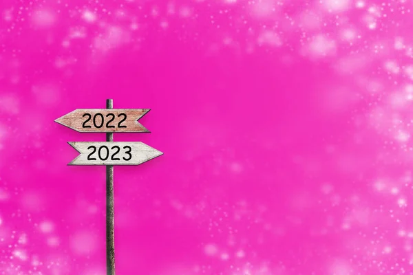 2022, 2023. Wooden sign with arrows pointing in different directions. Bright pink background.Right direction. Right choice. Plans for the New Year. New Year concept.