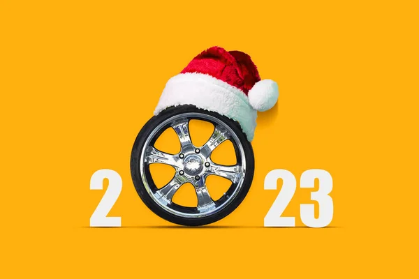 在明亮的橙色背景的圣诞老人帽的汽车车轮 复制空间 文字的位置 新年贺卡 节日背景 免版税图库照片