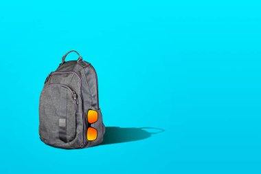 Mavi arka planda güneş gözlüğü olan bir sırt çantası. Uzayı kopyala Seyahat konsepti. Seyahat arkaplanı.