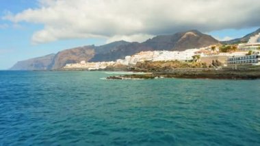 Nefes kesici hava manzaralı dramatik dağlar, mavi okyanus dalgaları kıyıya vuruyor. Gök mavisi deniz suyunun üzerinde uçan güzel bir hava aracı. Tropik ada Tenerife 'nin kayalık zirveleri. Suya yakın çekim.