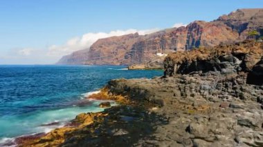 Erkek turistler volkanik Tenerife Adası 'ndaki kayalık plajdan okyanus manzarasının tadını çıkarırlar. Dalgalar köpük saçar. Giants uçurumları Acantilados de Los Gigantes. Yaz tatili. Hava aracı uçuşu. Hafta Sonu.