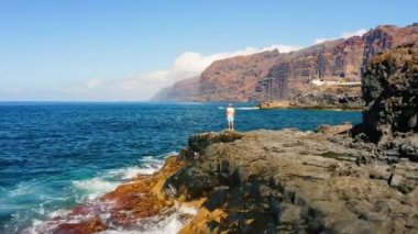 Erkek turistler volkanik Tenerife Adası 'ndaki kayalık plajdan okyanus manzarasının tadını çıkarırlar. Dalgalar köpük saçar. Giants uçurumları Acantilados de Los Gigantes. Yaz tatili. Hava aracı uçuşu. Hafta Sonu.