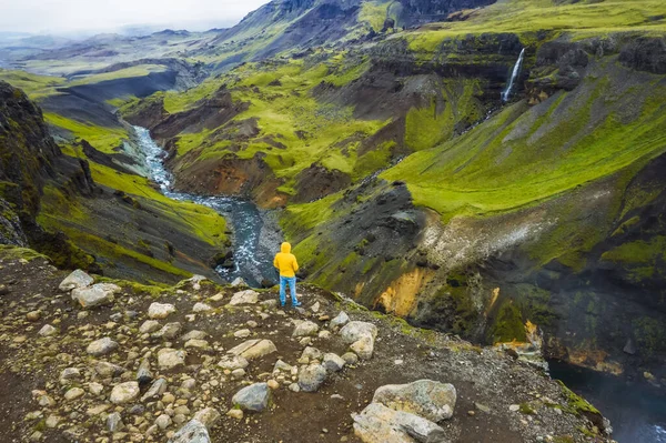 穿着黄色夹克的男人欣赏冰岛的高地 福萨河流经Landmannalaugar峡谷 山崖上覆盖着青苔 — 图库照片