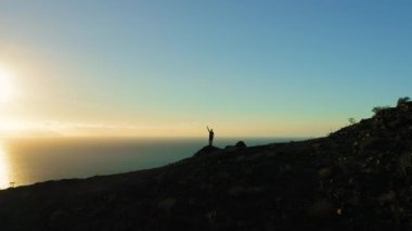 Yürüyüşçü dağın tepesindeki okyanus manzarasını sever. Uçurumun kenarında duran bir adam kolunu kaldırıyor. Başarı zafer başarısı. Kamera şahsi olarak hareket ediyor. Ünlü turistik bölge Los Gigantes