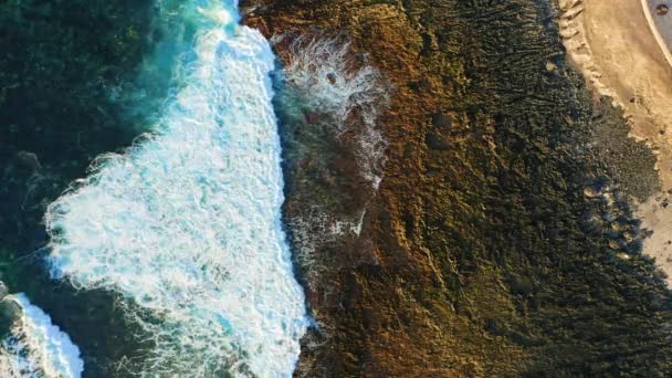 空旷的岩石火山海滩海浪冲撞着热带海岸并以火山岩形成泡沫 阳光灿烂的日子 野外遇上深蓝色清澈的海水 从上往下俯瞰 — 图库视频影像